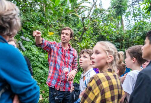 A group of school pupils standing looking in the direction of the teacher who is pointing